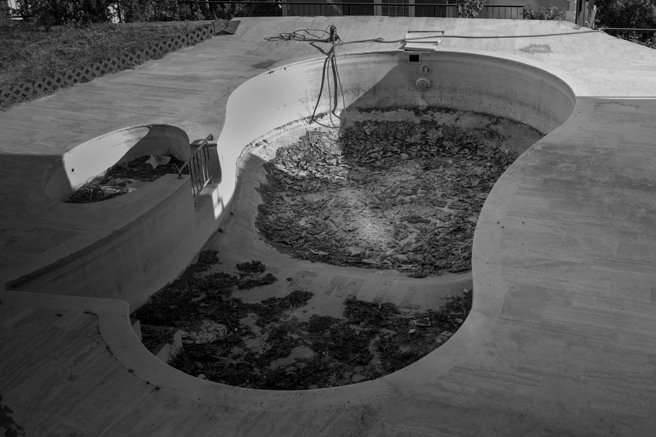 Black and white photo of a neglected empty swimming pool with debris.